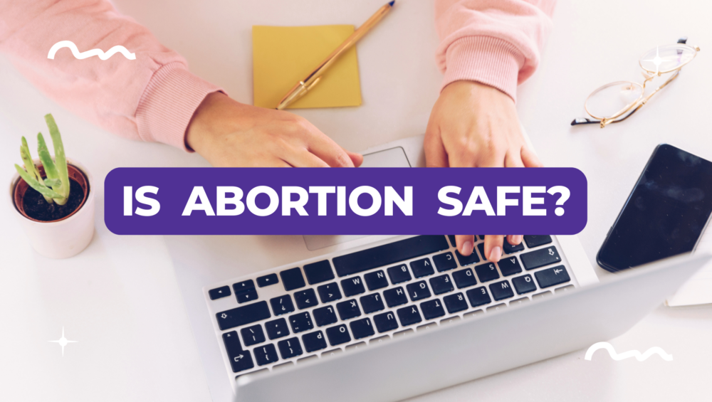 Young woman typing on a laptop with text overlay asking 'Is Abortion Safe?'